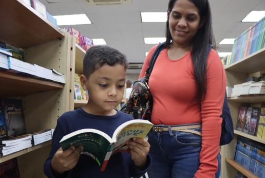 A migrant child reads a book while his mother looks on.