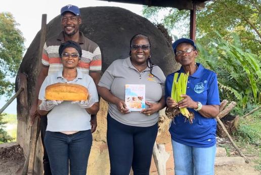 Four people standing with a loaf of bread and a traditional dirt oven in Tobago