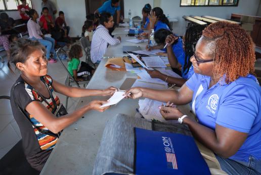 An IOM staff member speaks with a migrant at a food voucher distribution event