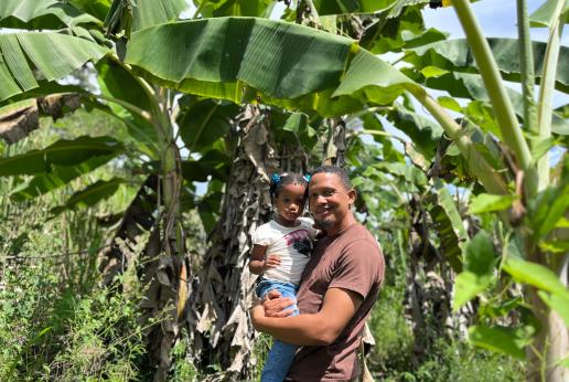 A father and daughter stand near a plantain tree
