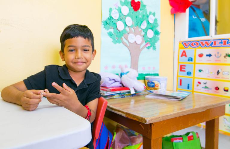 A child smiles while sitting in a pre-school classroom